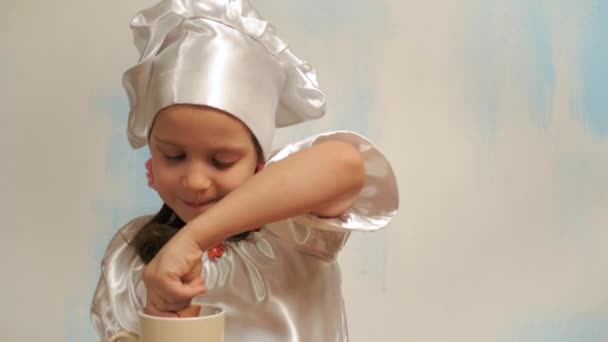 Menina em cap chef mergulha biscoito no leite. Mostrando polegar para cima — Vídeo de Stock