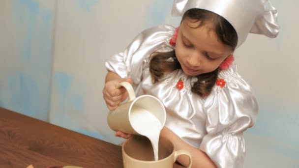 Menina no chapéu do chef derrama leite em uma xícara, close-up — Vídeo de Stock