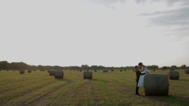 Gelin saman üzerinde oturur. Damat karısı günbatımında alanını sarılma..