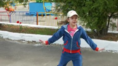 Kız bir eşofman ve parkta yeşil ağaçlar bir arka plan üzerinde dans şapka.