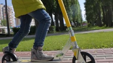 Küçük kız bir scooter sürme yeşil ceketli. Steadicam çekim. Ağır çekim