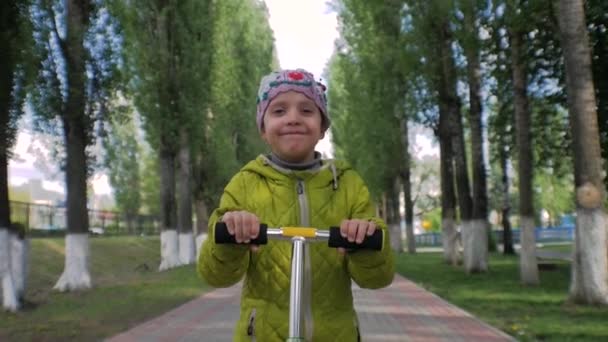 Petite menina monta uma scooter na câmera. Cara sorridente. Movimento lento . — Vídeo de Stock