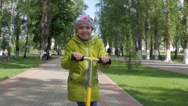 Petite fille monte un scooter sur la caméra. Visage souriant. Mouvement lent . — Video