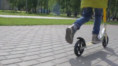 Yeşil ceket ve kot kaldırımda bir scooter sürme, küçük kız. Steadicam çekim. Ağır çekim.