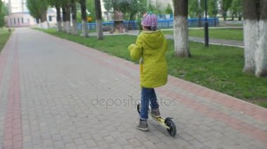 Küçük kız bir scooter sürme yeşil ceketli. Steadicam çekim.