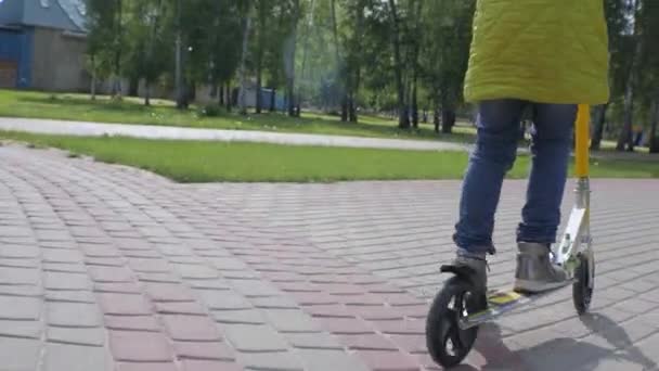 歩道でスクーターに乗っている緑のジャケットとジーンズの女の子 シュテアディカムを撃つ — ストック動画