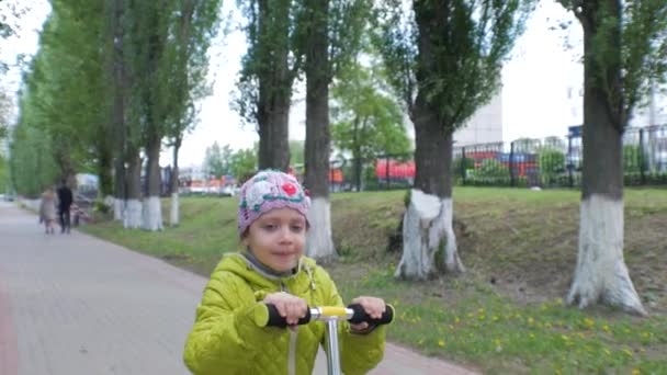 Petite κορίτσι βόλτες ένα σκούτερ για τη φωτογραφική μηχανή. Χαμογελαστό πρόσωπο. Αργή κίνηση. — Αρχείο Βίντεο