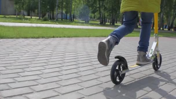 Petite fille en veste verte et jeans chevauchant un scooter sur le trottoir. Tir sur Steadicam. Mouvement lent . — Video