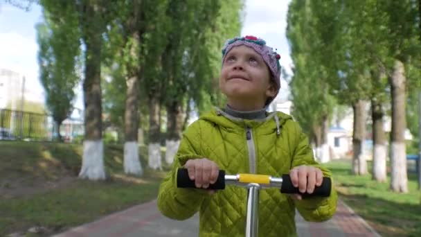 Маленька дівчинка катається на скутері на камеру. Усміхнене обличчя . — стокове відео