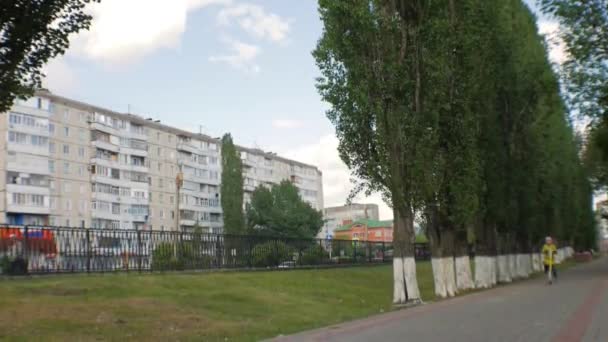 Petite fille en veste verte et jeans chevauchant un scooter sur le trottoir. Prise de vue Steadicam . — Video