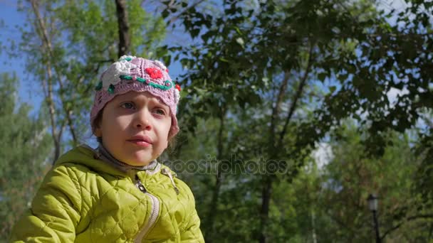 Het meisje kauwt op een achtergrond van groen gebladerte van bomen. — Stockvideo