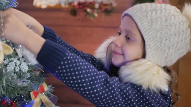 Young girl in hat putting ornament on Christmas tree — Stock Video