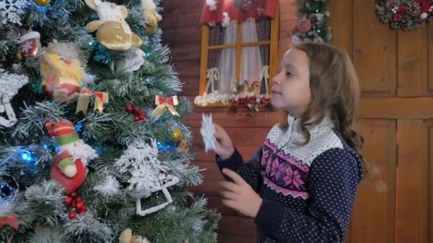 Ung flicka i hatt att sätta prydnad på julgran — Stockvideo