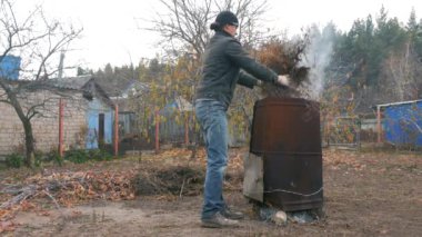 Adamın biri metal bir fıçıda çöp yakıyor. Kuru ot ve organik atık yanar ve duman çıkarır. Bahçede sonbahar işi.