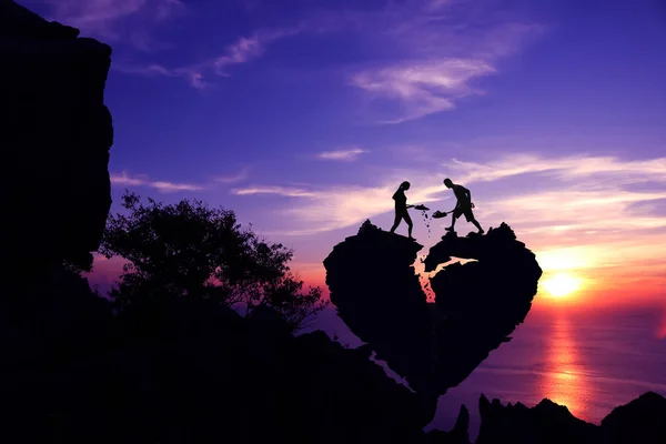 Valentine day,Silhouette Couple helping to shoveling stone for repair the broken heart shape rock on the mountain. — Stock Photo, Image