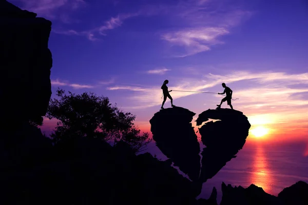 Silhouette alla hjärtans dag, par drar repet på trasiga hjärtformad sten på ett berg. — Stockfoto