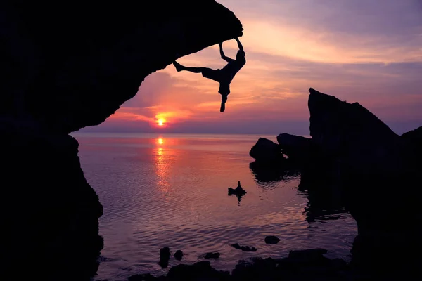 Man klimmen op de rotsen in de buurt van de zee met paarse hemel zonsondergang. — Stockfoto