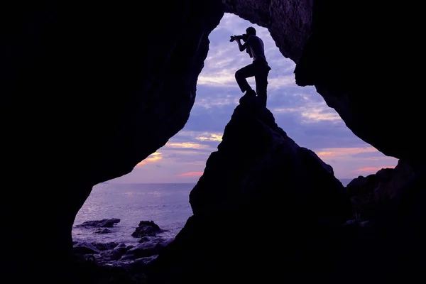 Fotograaf voor de grot in de buurt van de zee met paarse sky. — Stockfoto