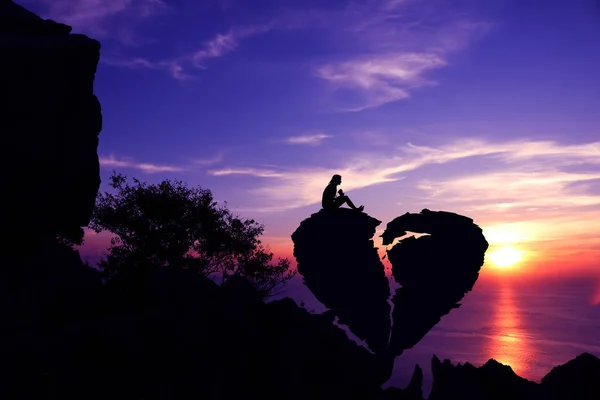 Día de San Valentín, las mujeres se sientan en una piedra rota en forma de corazón en una montaña con fondo de atardecer cielo púrpura . —  Fotos de Stock