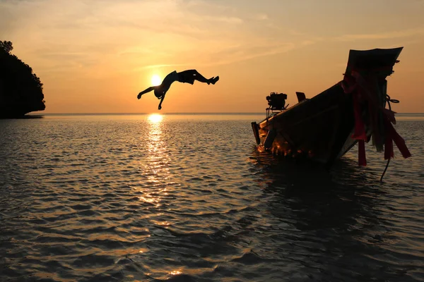 Silhouette filles sauter d'un bateau dans la mer épisode coucher de soleil, Somersault à l'océan — Photo