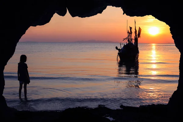 Silhouette girls stands in front of the cave by the sea with local fishing boats. — Stock Photo, Image