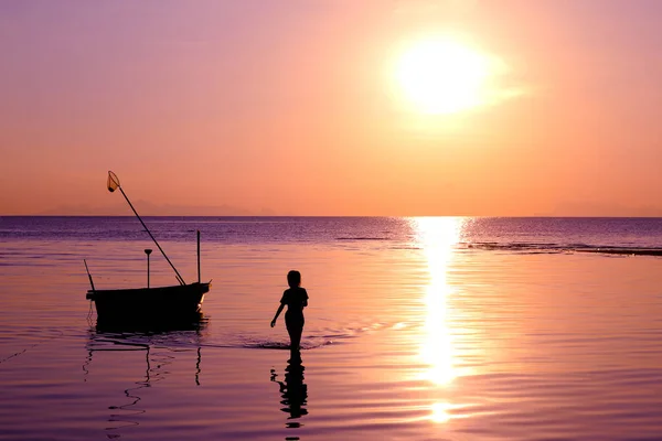 Silueta chica caminó en la playa con un barco de pesca y puesta de sol . — Foto de Stock