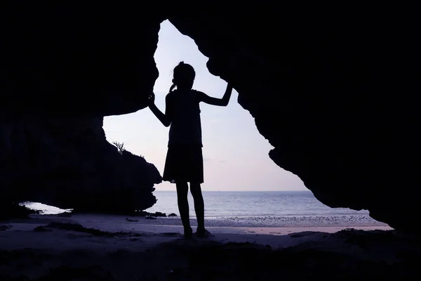 Silueta niñas de pie en frente de una cueva en la playa . —  Fotos de Stock
