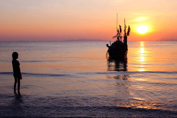 Silhouette fille a marché sur la plage avec un bateau de pêche et coucher de soleil . — Photo