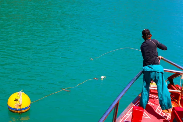 A man throws a rope to tie up the boat with buoys.