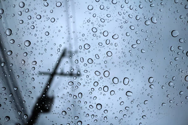 Regentropfen auf Glas mit blauem Himmel und Lichtmasten. — Stockfoto
