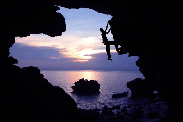 Fotógrafo escalando roca en la cueva cerca de la playa con puesta de sol cielo púrpura . — Foto de Stock