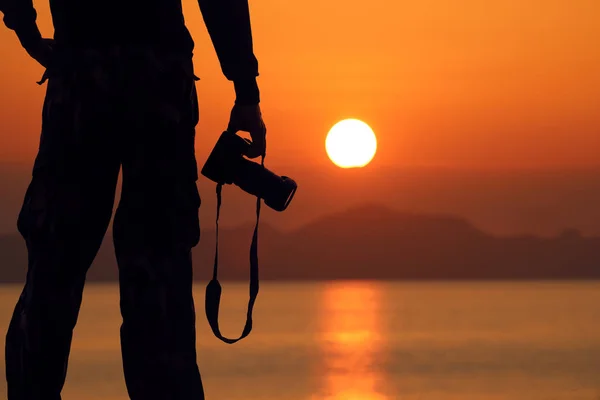 Silhouette of a photographer holding professional camera on the — Stock Photo, Image