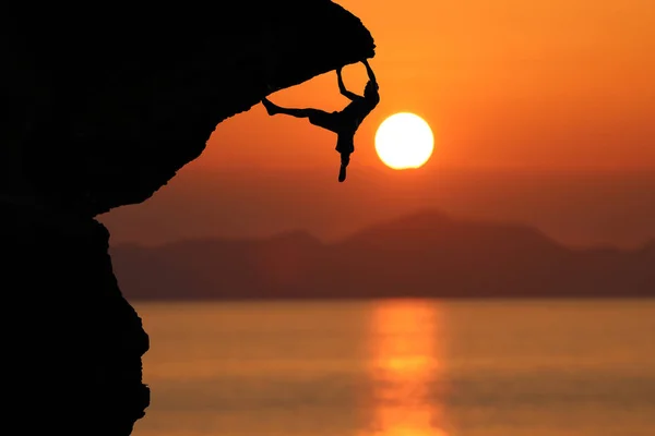 Силуэт альпиниста на скале против красивого красного неба солнца — стоковое фото