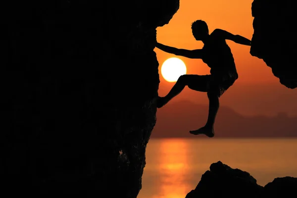 Силуэт альпиниста на скале против красивого красного неба солнца — стоковое фото