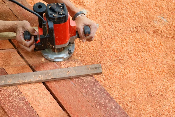 Workers using electric routering on the wood and sawdust