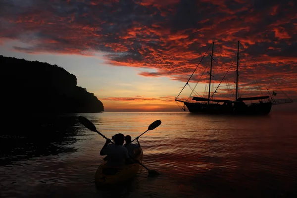 Mother and daughter kayaking back to the yacht with red sky suns — Stock Photo, Image