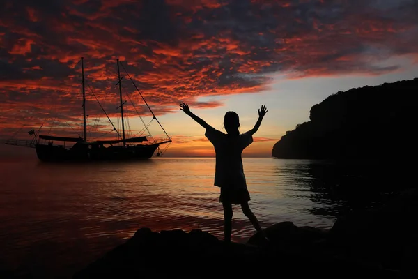 Chica estirar los brazos en las rocas y yate con el cielo rojo en el — Foto de Stock