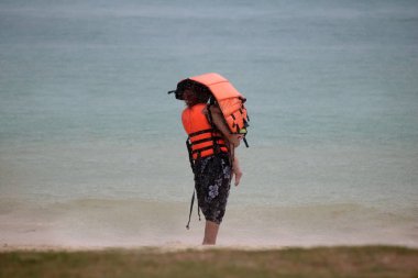 Şemsiye ve yağmurluk ya da can yelekleri sahilde turistler