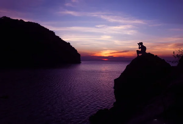 海によって岩の上にカメラを使用して写真家のシルエット 夕暮れの空の背景 — ストック写真
