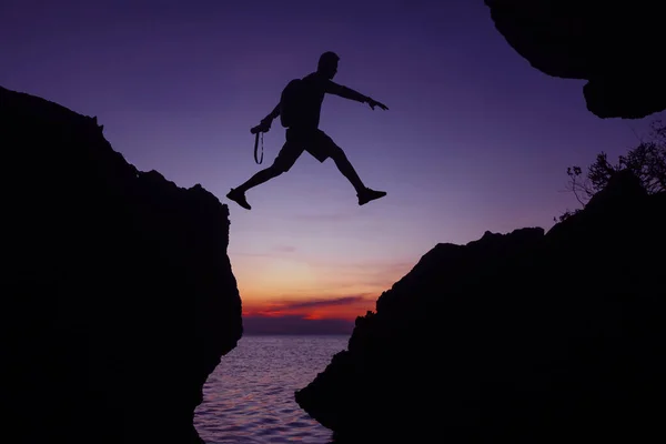 Silhouette of the photographer jumping over the stone at sunset ,Man Jumping between rocks on tropical Sea at twilight sky background.