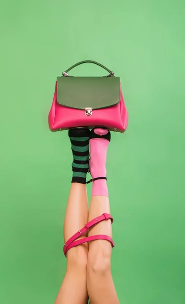 Zenske nohy drží kabelku na zeleném pozadí — Stock fotografie