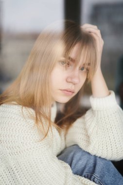 Cazibeli sarışın ergen, depresyonda, pencerenin yanında oturuyor. Stresli, yalnız ya da kederli durum kavramı