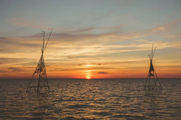 Silhouettes of tree sticks construction in the water with beautiful tranquil summer scene of orange sunset above the sea. Seascape like a heaven concept