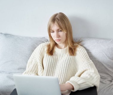 Dizüstü bilgisayarla çalışan, beyaz kazaklı hippi kız ve kot pantolonlu modern not defteri kullanarak bir yatakta oturan sevimli genç bayan yönetici. Karantina sırasında çevrimiçi çalışma, öğrenim veya serbest çalışma kavramı