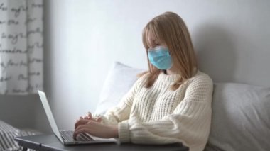 Medikal maskeli çekici bir kadın, evinde dizüstü bilgisayarla çalışıyor. Virüs hastalıkları sırasında karantinadaki defter ya da bilgisayar kullanarak çalışma, öğrenme, sörf yapma, sohbet etme kavramı