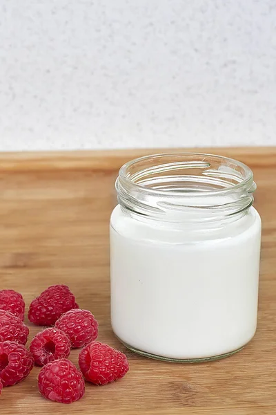 Yogurt dalam botol kaca dan raspberry pada latar belakang kayu — Stok Foto