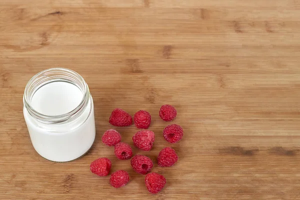 Yogurt dalam toples kaca dan raspberry pada latar belakang kayu - templat tiruan — Stok Foto