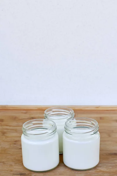 Três jarros de vidro com iogurte em um fundo de madeira - vertical — Fotografia de Stock