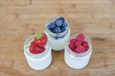 Yoğurt ve ahşap arka plan üzerinde meyveleri ile üç Cam Kavanoz