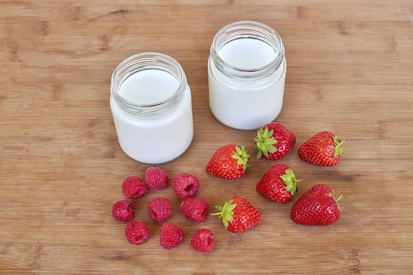 Yogurt dalam botol kaca, raspberry dan stroberi pada latar belakang kayu — Stok Foto